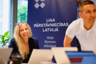 Foto no LIAA pasākuma, kurā redzams organizācijas nosaukums un otrajā plānā divas personas