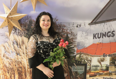 Līga Kricka ar ziediem uz pilsētas māju fona