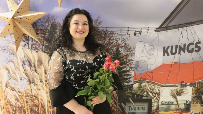 Līga Kricka ar ziediem uz pilsētas māju fona