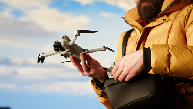 Persona dzeltenā virsjakā tur rokās dronu
