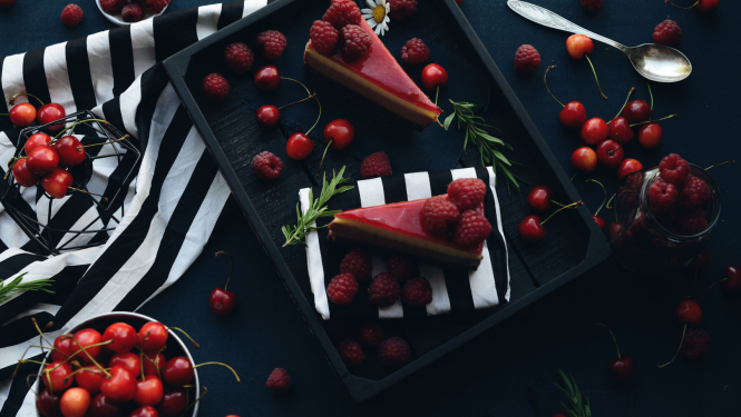 Sarkanas kūciņas uz melna šķīvja, viss izdekorēts ar sarkanām ķiršogām