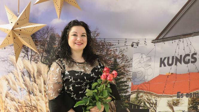 Līga Kricka ar ziediem uz pilsētas māju fona