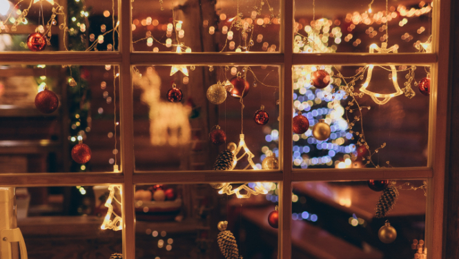 Skaisti izrotāts logs Ziemassvētku noskaņās. Ar lampiņām, sarakanām bumbiņām un egles atspulgu.