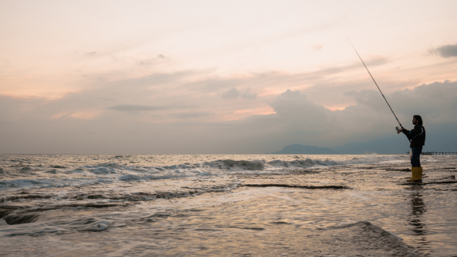 Cilvēks, kas saulrieta laikā, zvejo jūrā.