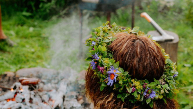 Meitene ar pļavu puķu vainadziņu pie ugunskura